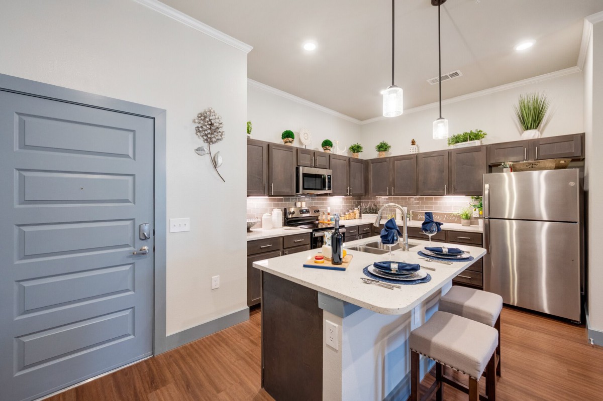 A modern kitchen with a central island featuring bar stools and stylish hanging lights.
