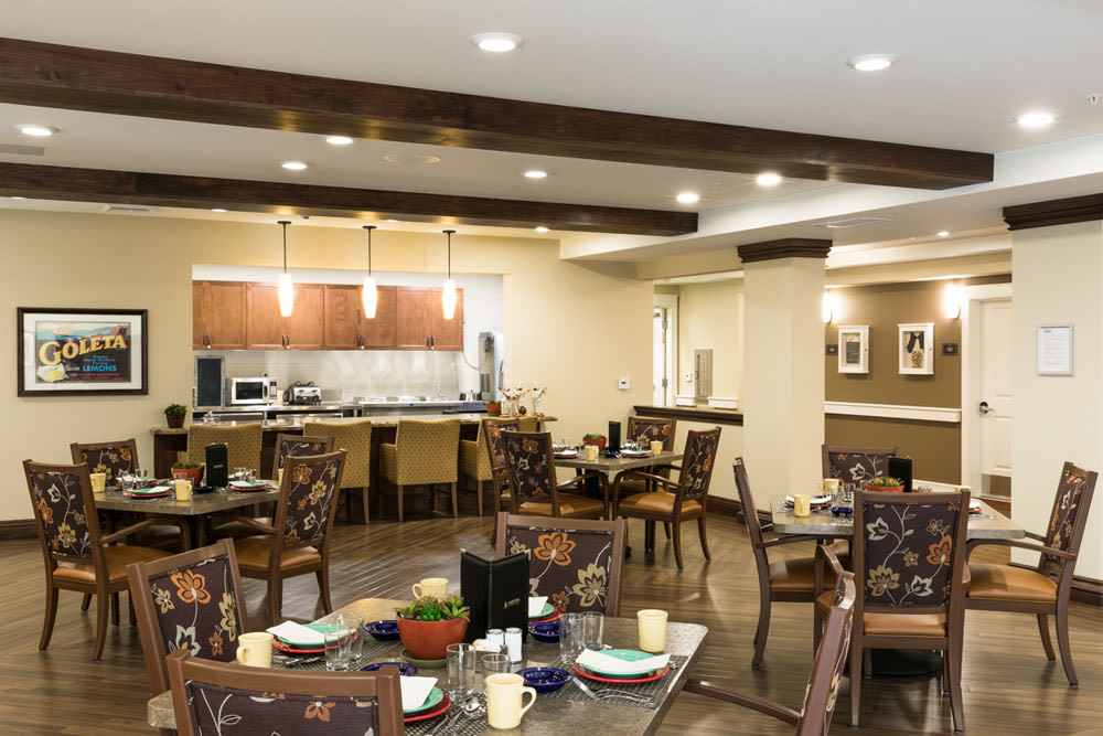 A cozy dining area with elegantly set tables and chairs, featuring an open kitchen design.