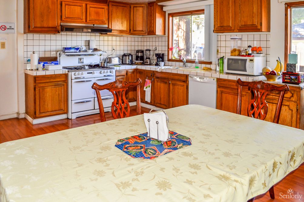 A cozy kitchen featuring wooden cabinets, a dining table with a colorful mat, and various kitchen appliances.