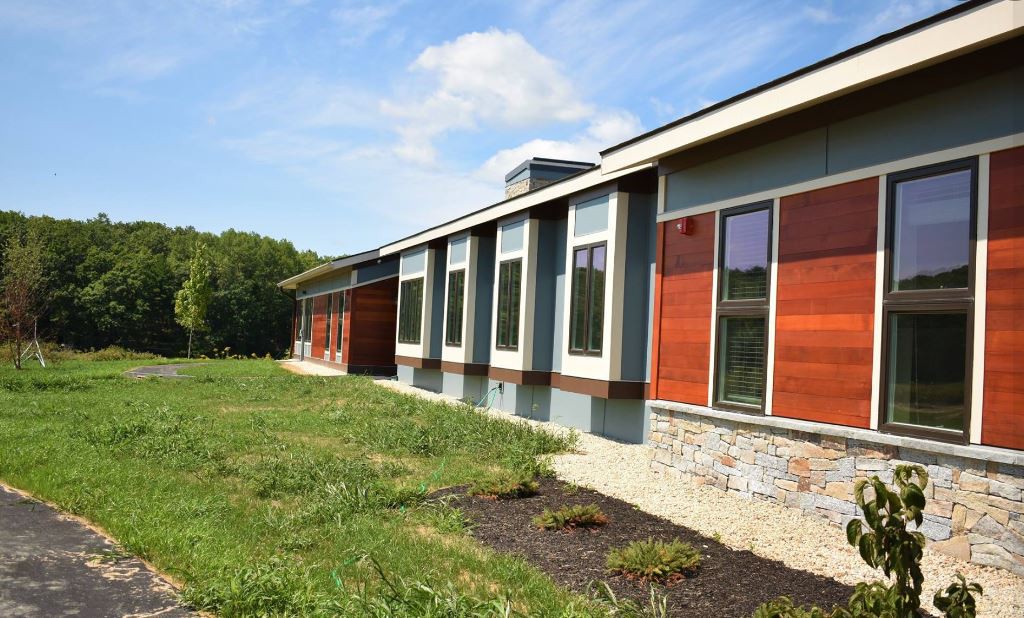 A modern building with large windows set against a backdrop of green landscape on a sunny day.