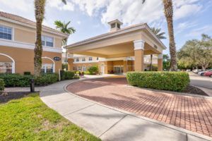 A sunny entrance to a building with a covered driveway and palm trees.