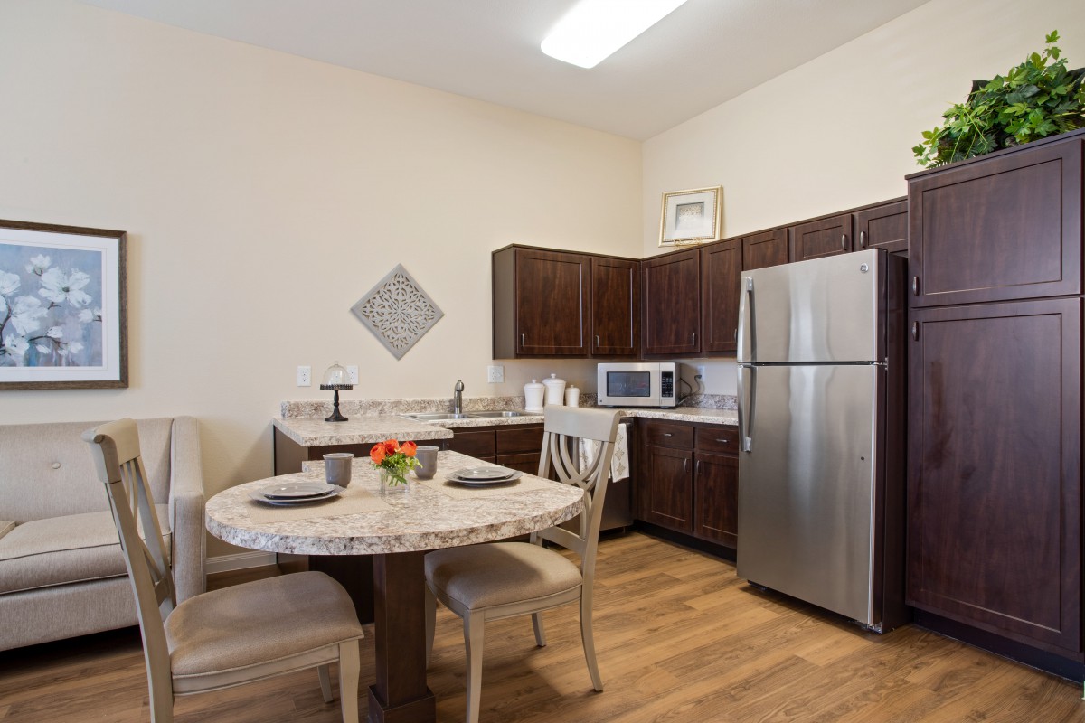 A modern kitchen with a dining area featuring a round table and chairs, stainless steel refrigerator, microwave, and brown cabinets.