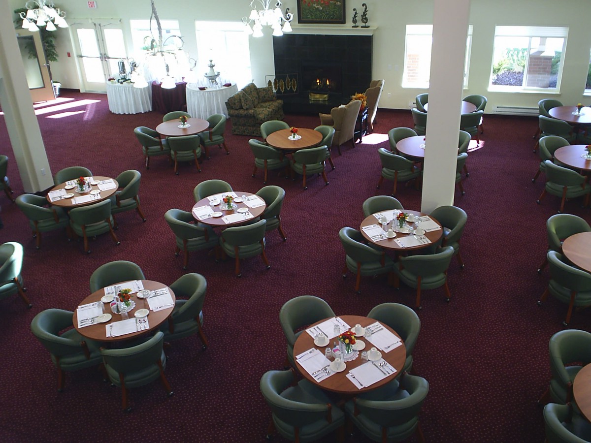 Empty dining area with round tables and chairs on a carpeted floor.