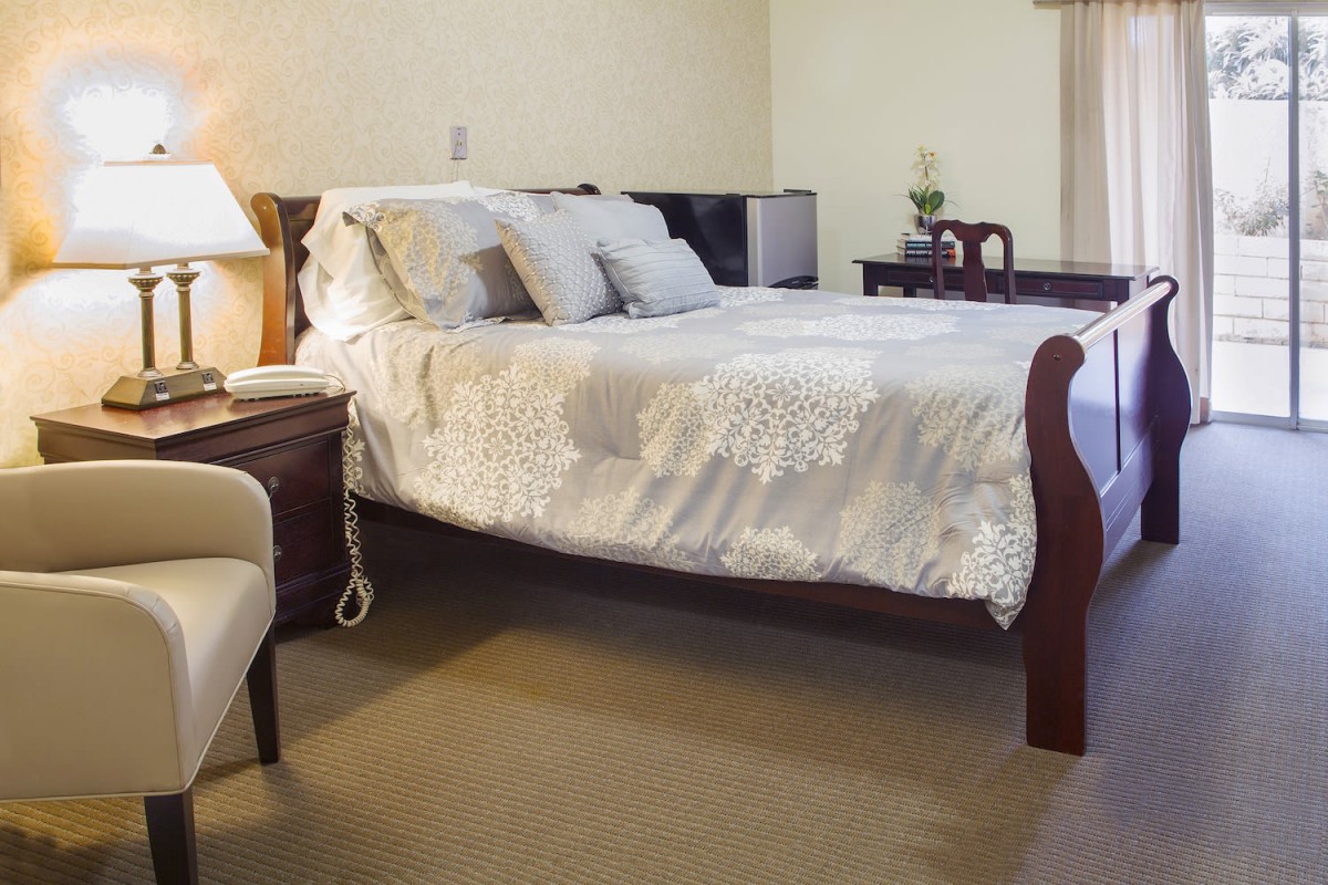 A cozy bedroom featuring a large bed with multiple pillows, a nightstand with a lamp, and elegant decor.
