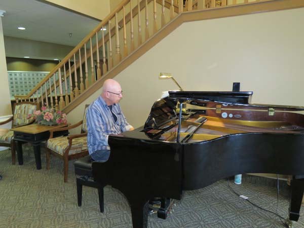 A person playing a grand piano indoors near a staircase.