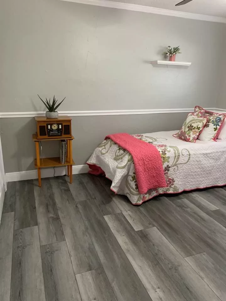 A cozy bedroom with a single bed featuring floral bedding and a pink blanket, complemented by a wooden nightstand and minimalistic decor.