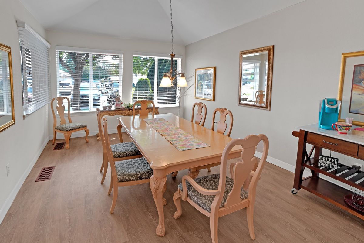 A bright dining room featuring a wooden table with matching chairs, pendant lighting, and large windows offering natural light.