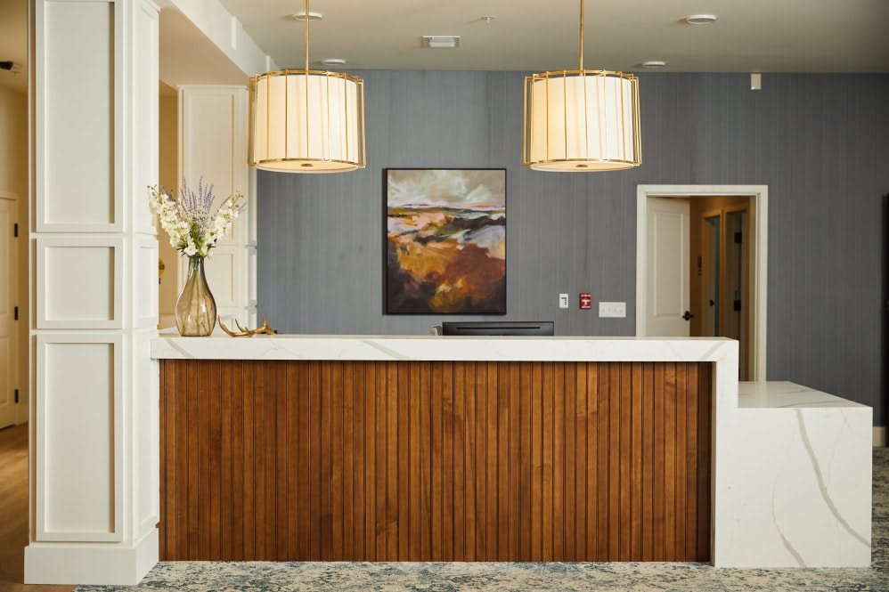 A modern hotel reception area featuring a wooden desk, pendant lights, and stylish artwork.