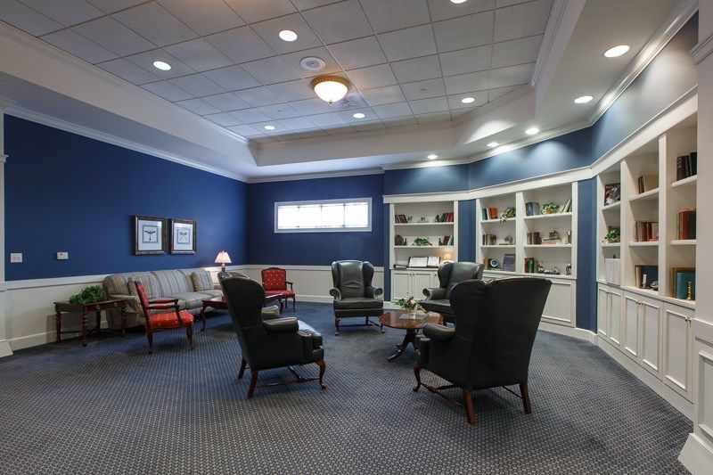 A cozy living room with a seating area featuring various chairs, sofas, and bookshelves against blue walls.