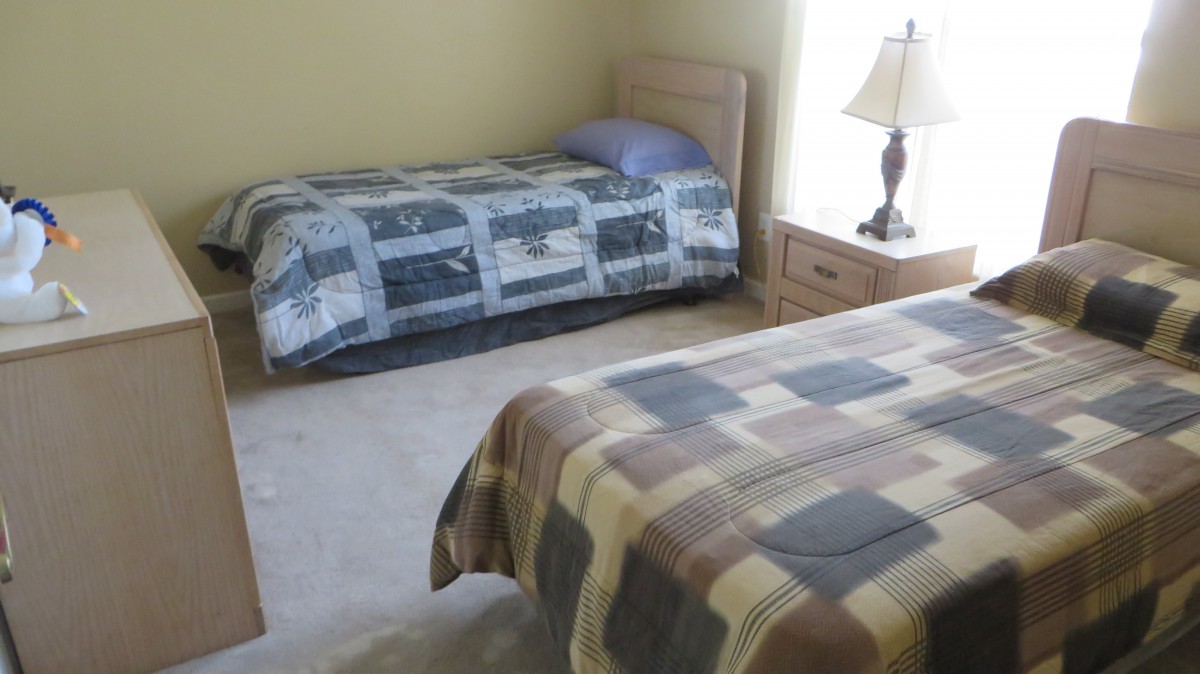 A bedroom with two twin beds and a nightstand with a lamp.