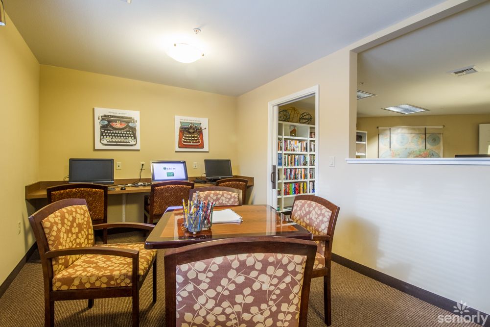 A cozy office space with computers, a table, chairs, and a small library.