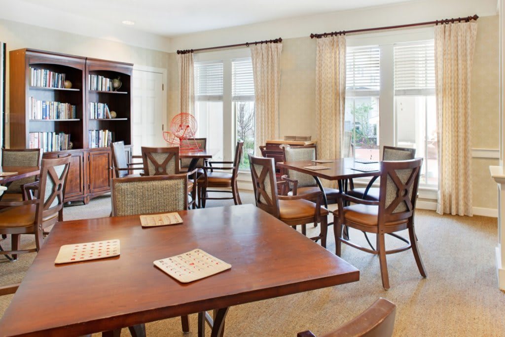 A well-lit dining room with wooden tables and chairs, complemented by large windows and curtains.
