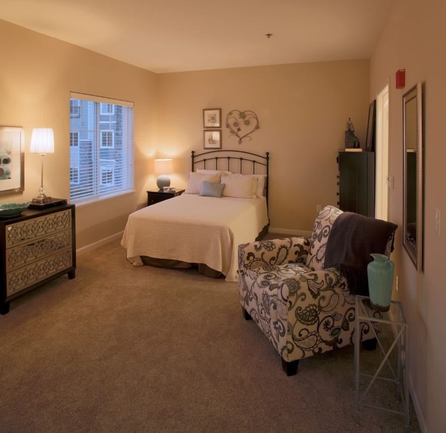 A cozy bedroom with warm lighting, featuring a bed, armchair, and stylish decor.