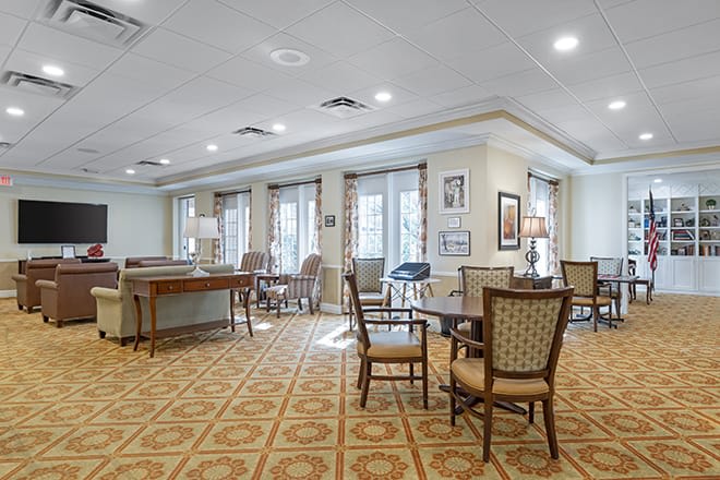 A spacious and well-lit seating area with tables and chairs arranged on a patterned carpet.