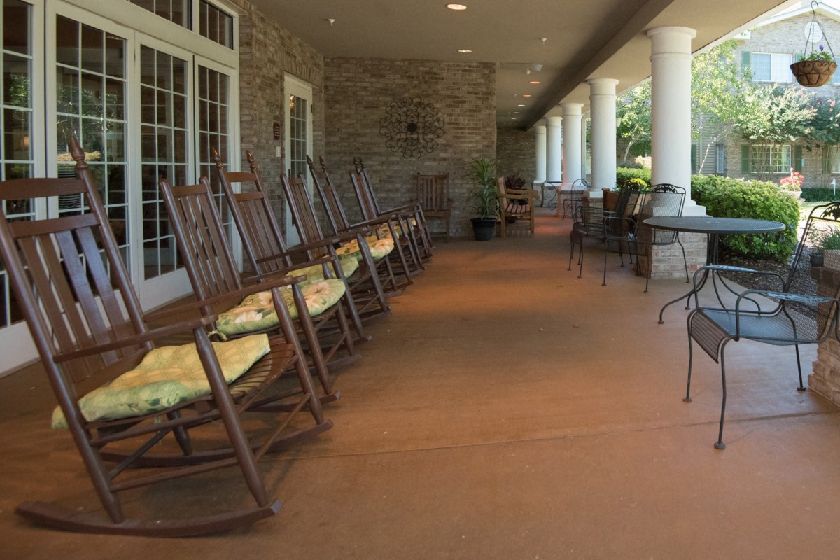 A spacious porch with a row of rocking chairs and stone walls, offering a relaxing outdoor seating area.