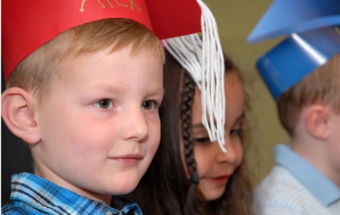Two children wearing graduation hats at a ceremony.