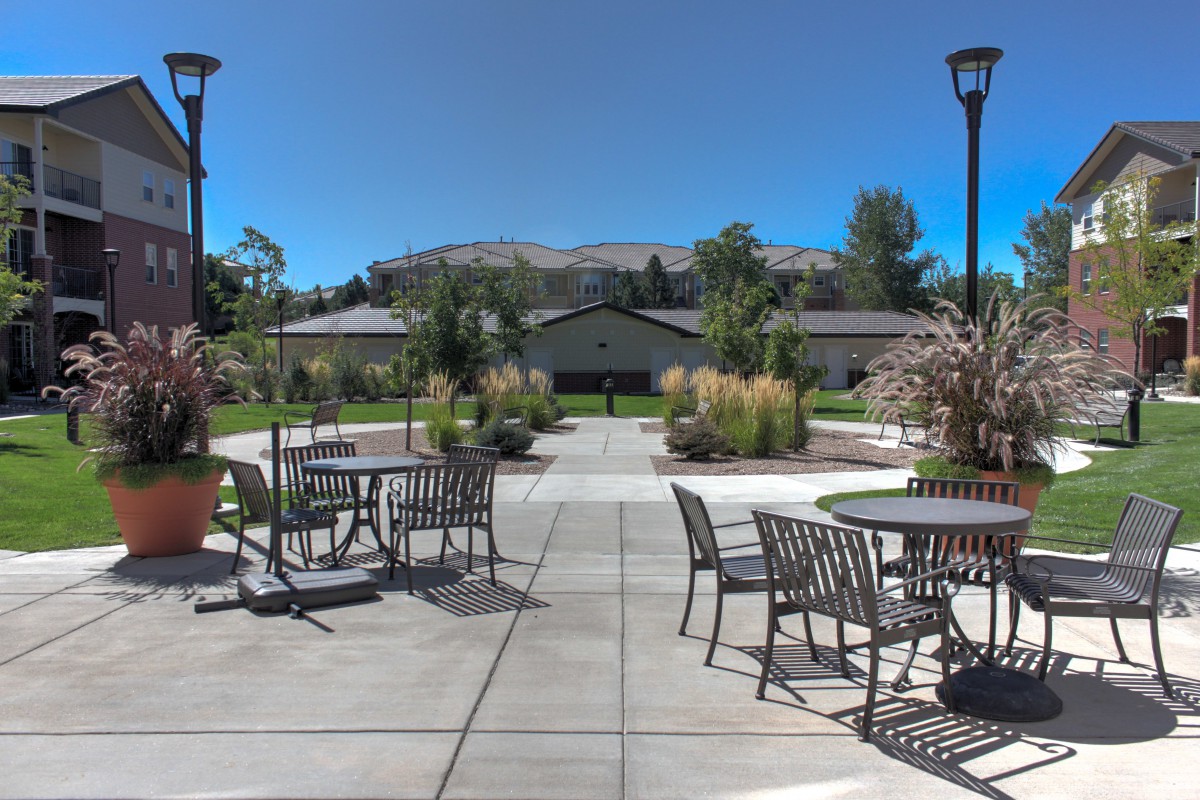 A peaceful outdoor patio area with tables and chairs, surrounded by a landscaped garden and trees.