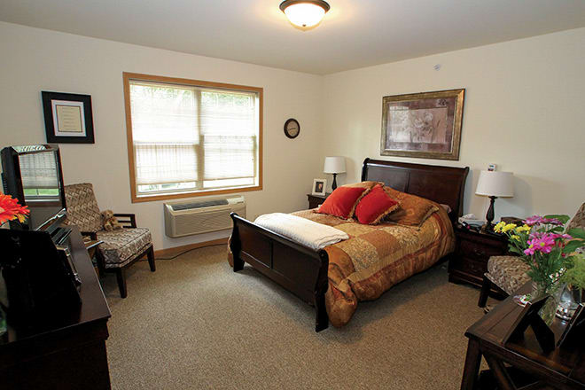 A cozy bedroom with a neatly made bed, wooden furniture, and natural light from the window.