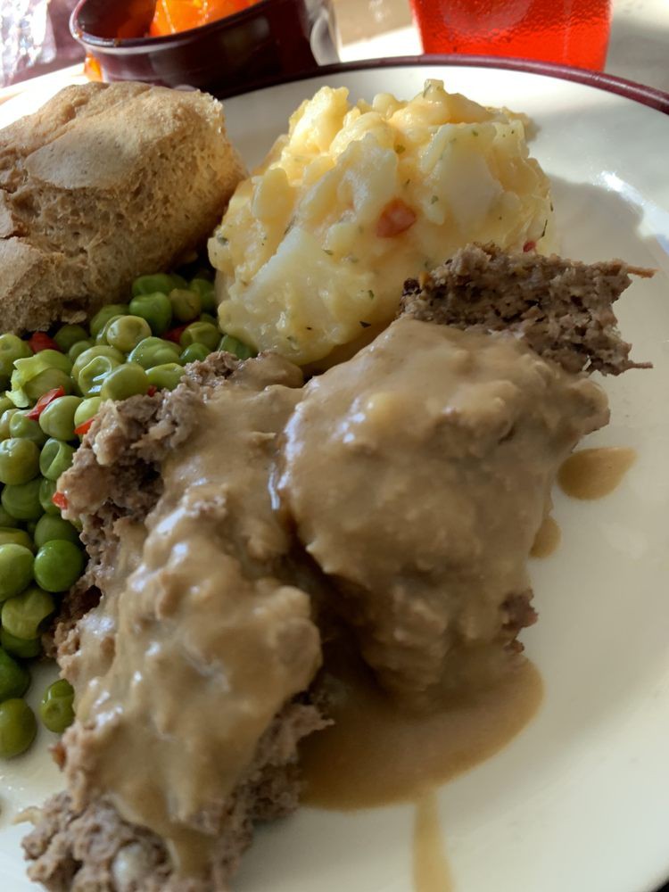 A hearty dinner with meatloaf, gravy, peas, and mashed potatoes.