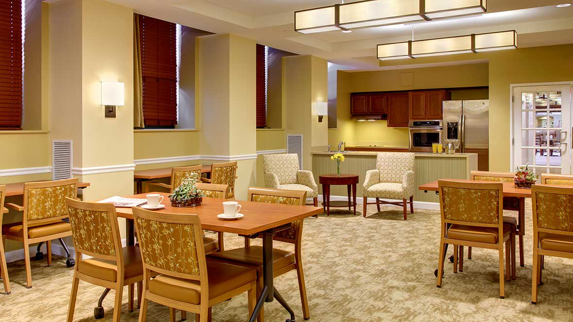 A modern dining area with wooden tables and chairs, adjacent to a kitchen.