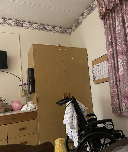 A patient room featuring a wheelchair, a television mounted on the wall, and a storage cabinet.
