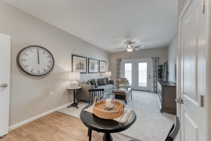 A cozy living room with modern furniture and decor, featuring a large wall clock and framed artwork.