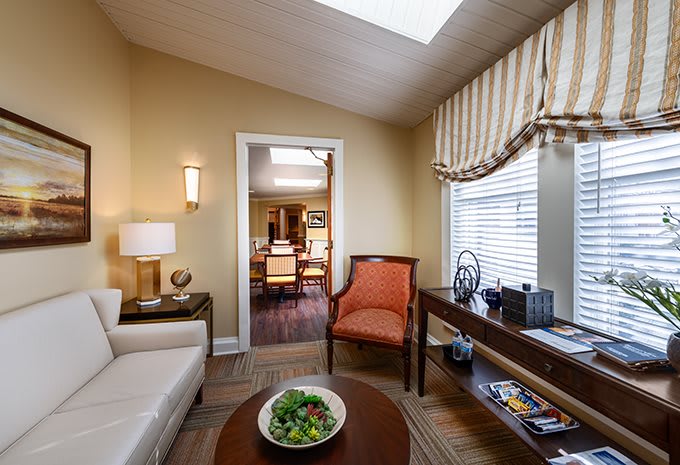 A cozy living room with a sofa, armchair, and elegant decor, featuring a window with striped curtains.