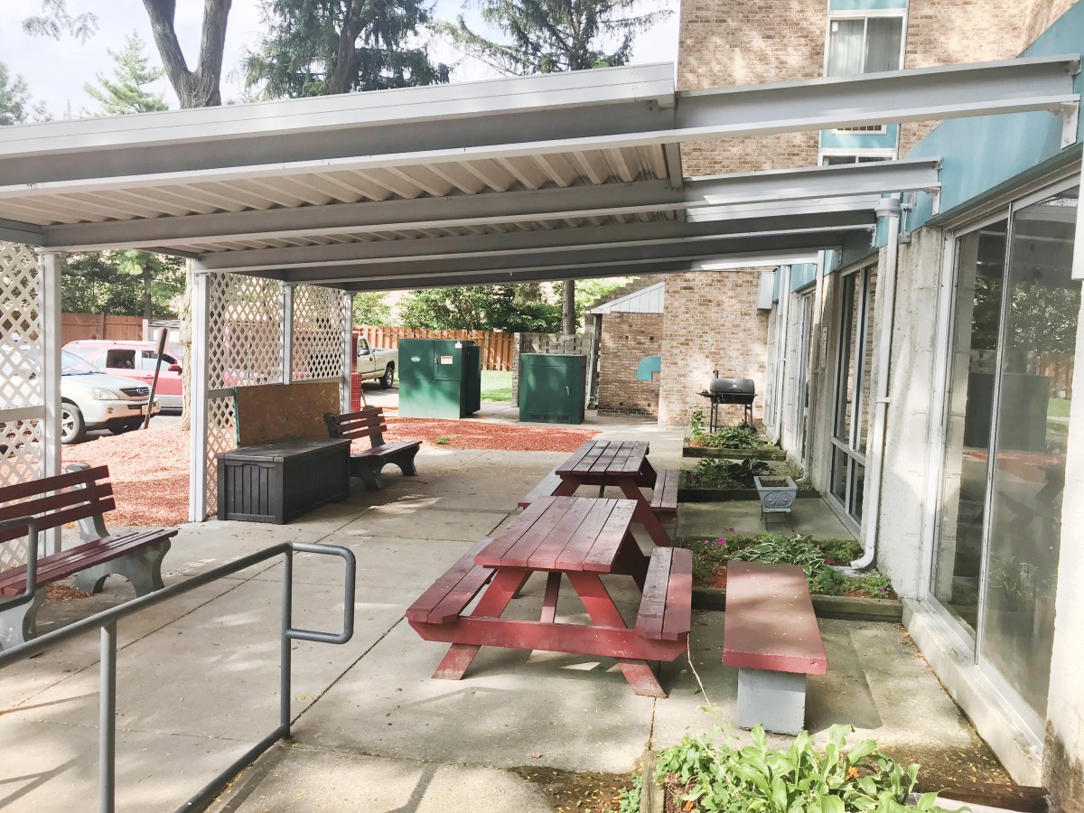 Covered outdoor seating area with picnic tables and benches in an urban environment.