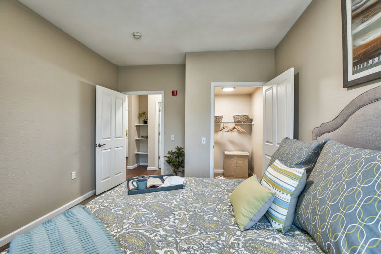 A modern bedroom with a neutral color palette, featuring a neatly made bed with decorative pillows and an open closet.