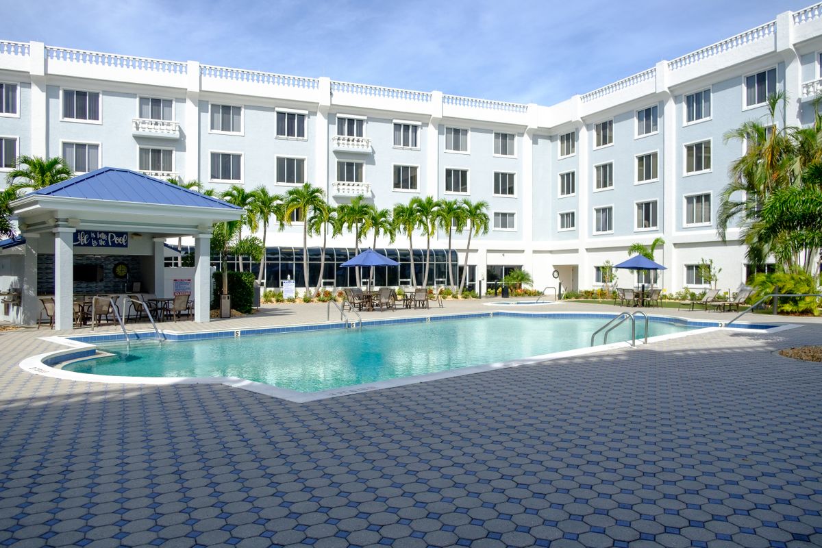 A hotel with an outdoor swimming pool surrounded by palm trees.