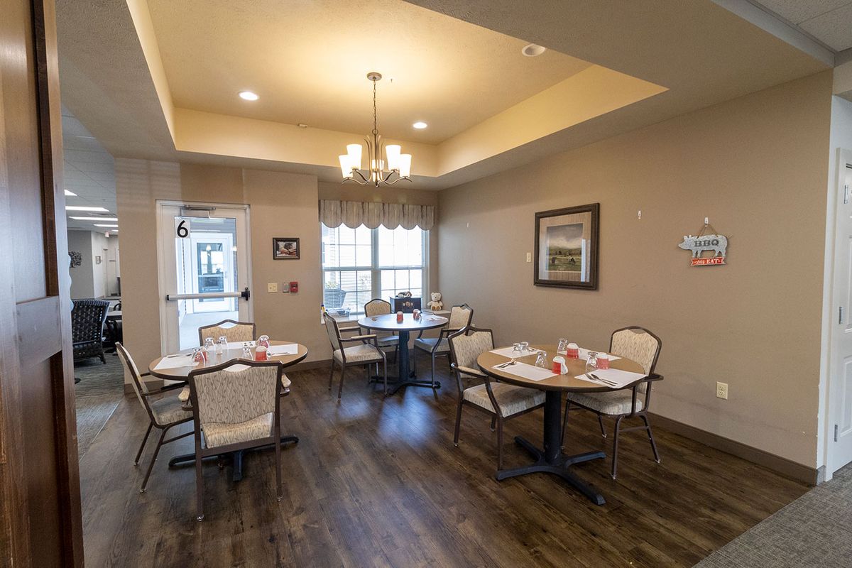 An elegantly set dining area with multiple tables and chairs, illuminated by a chandelier.