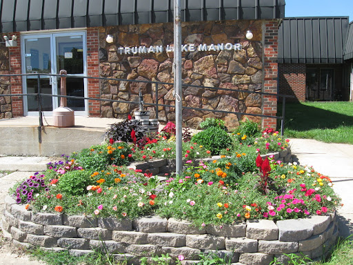 A vibrant garden blooms in front of a stone-faced building, complete with a flagpole.