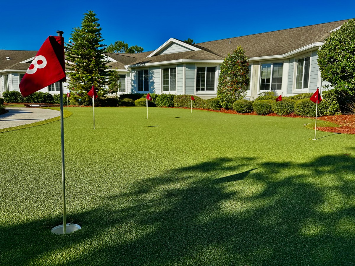 A putting green in front of a residential building on a sunny day.