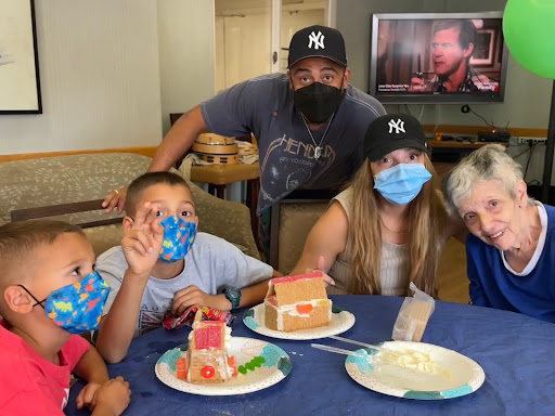 A joyful family gathering with children showcasing their gingerbread houses while wearing masks.