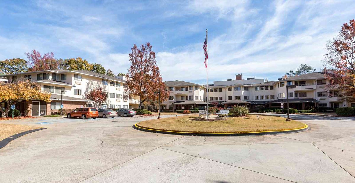 A three-story building with an American flag in front, surrounded by trees and a parking lot under a partly cloudy sky.