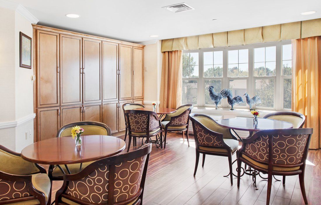 A bright dining area with several tables and chairs, illuminated by natural light from the large window.