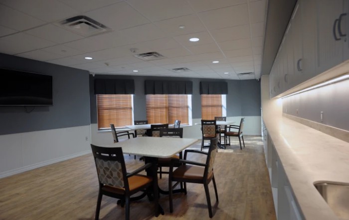 A dining area with multiple tables and chairs, featuring large windows and wooden flooring.