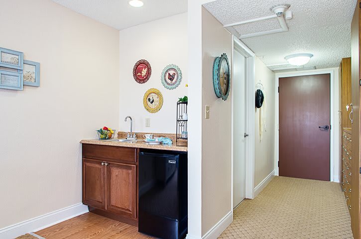 A small kitchenette area with wall-mounted decorative plates and a mini fridge next to a hallway.