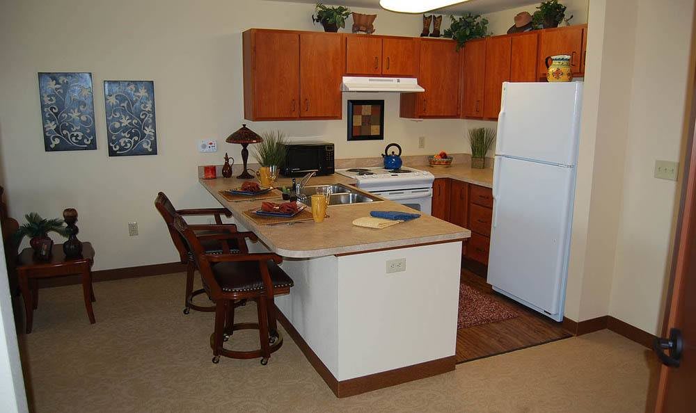 A cozy kitchen with wooden cabinets, a refrigerator, and a counter with stools.