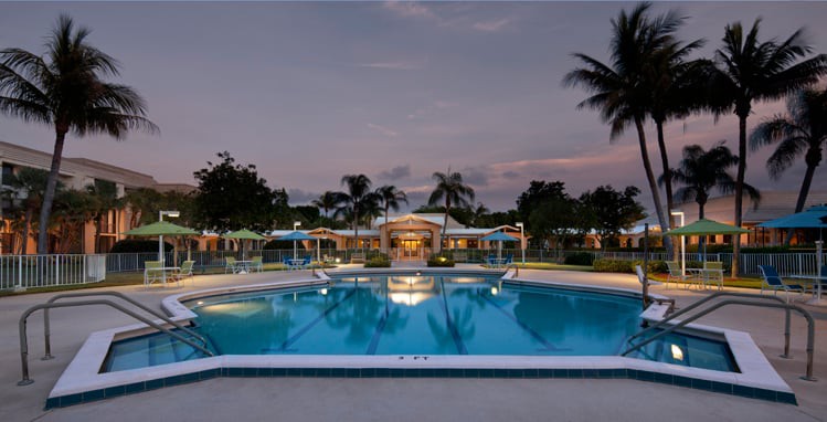 A tranquil evening view of a resort swimming pool surrounded by palm trees.