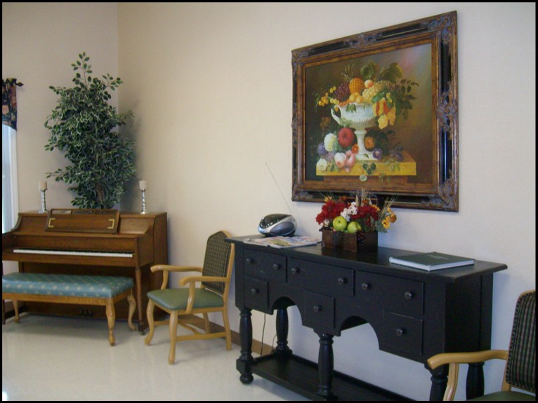 A cozy room interior featuring a small piano, elegant furniture, and a vibrant still-life painting on the wall.