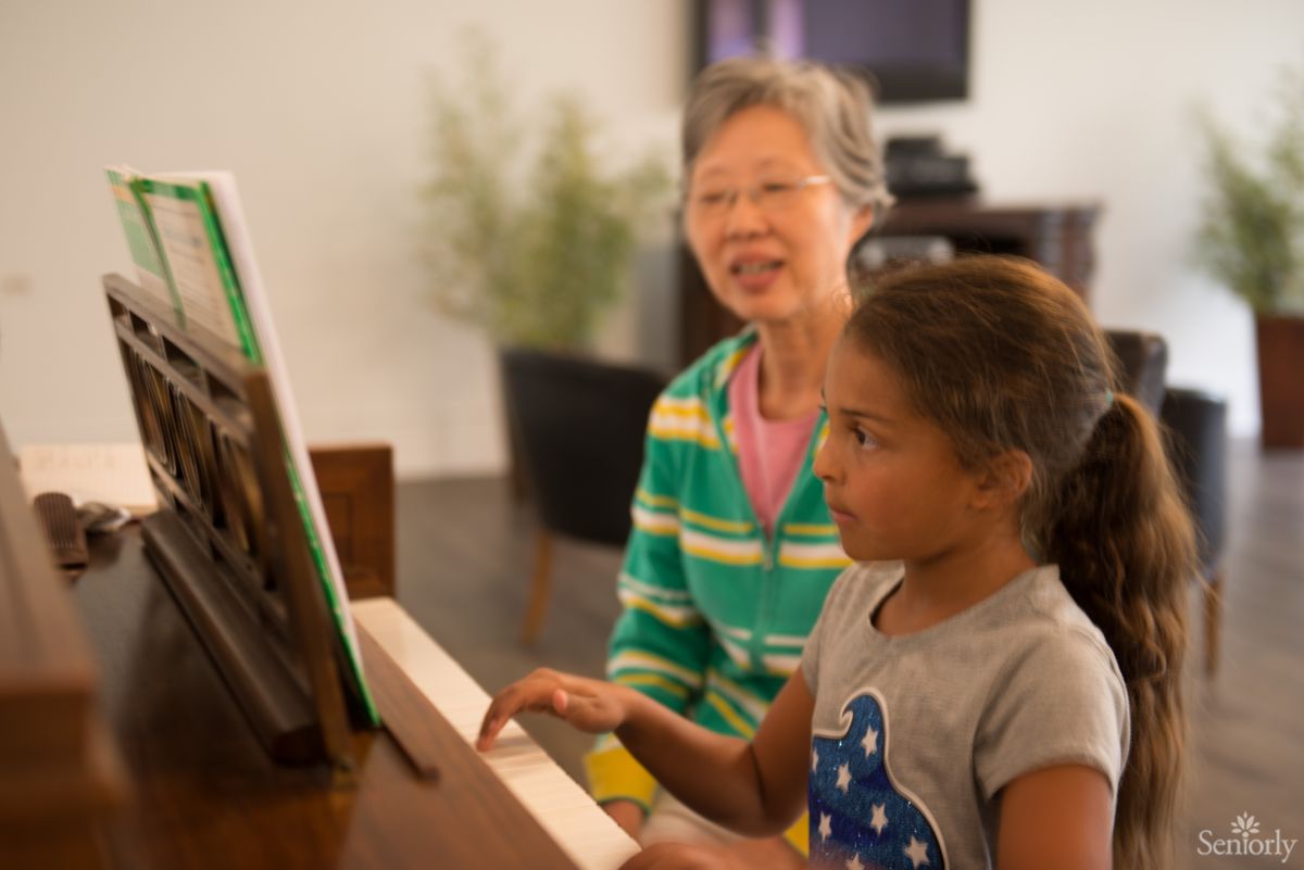 A music lesson in progress with a teacher guiding a young student at the piano.