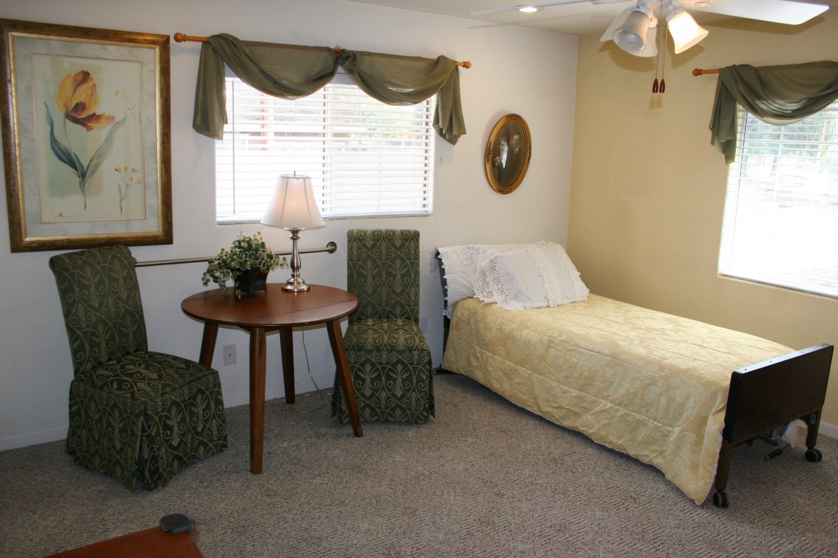 A cozy bedroom with a single bed, a small round table, and two chairs near a window with curtains.