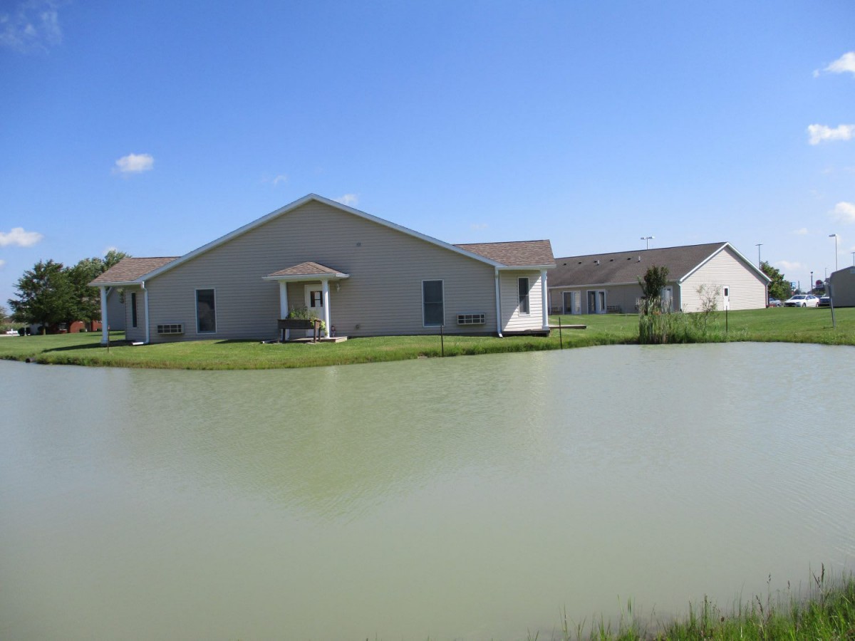 A house by a pond under a clear blue sky.