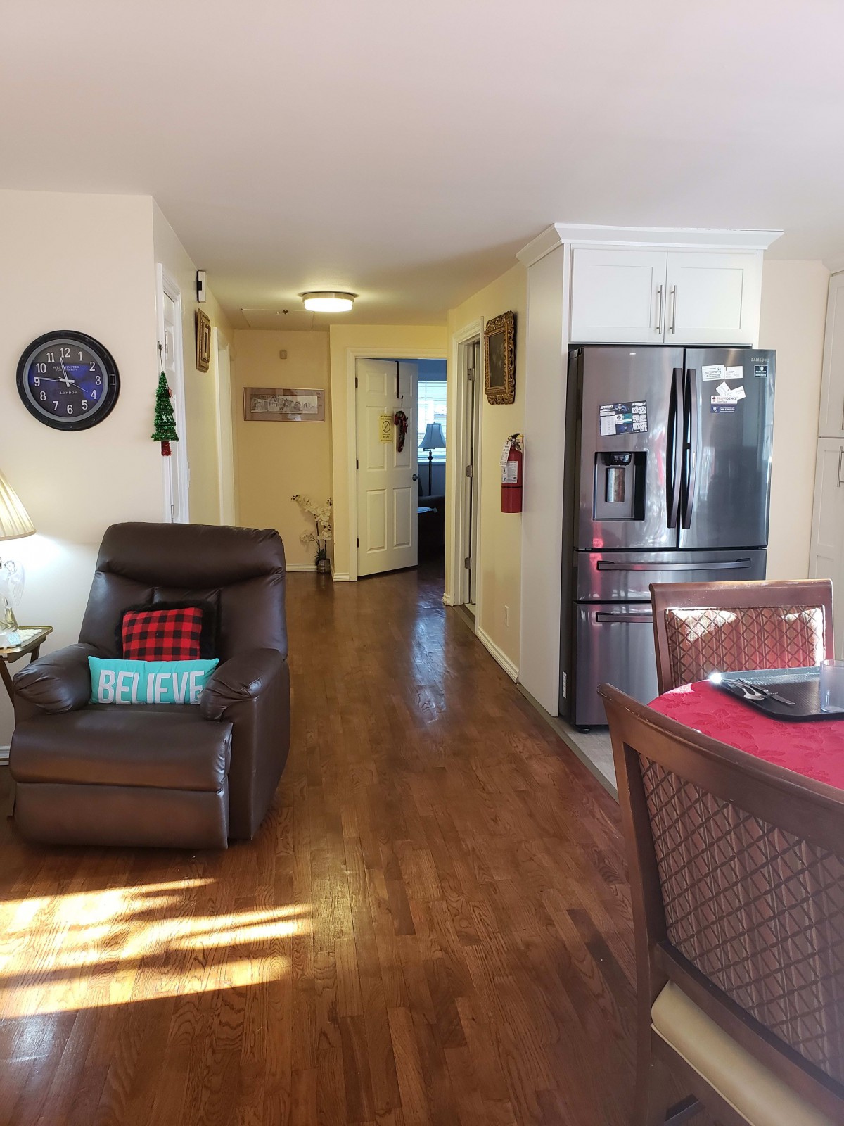 A cozy living space with a leather armchair, hardwood flooring, and an adjacent kitchen with a modern refrigerator.