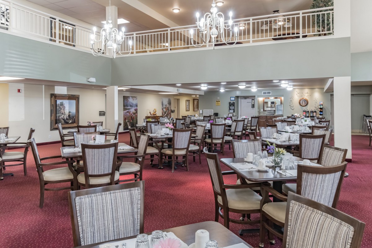 An elegant dining area featuring multiple tables and chairs, complete with chandeliers and a carpeted floor.