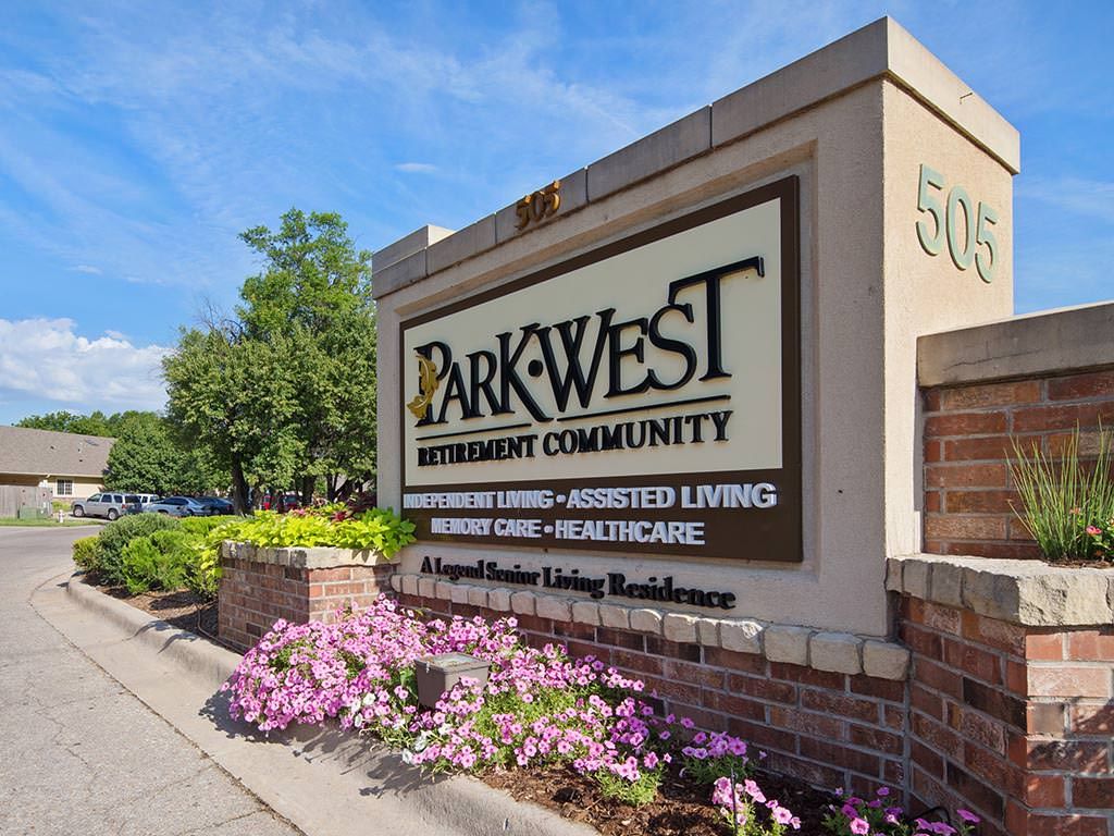 Entrance sign for Park West Retirement Community surrounded by flowers and greenery.