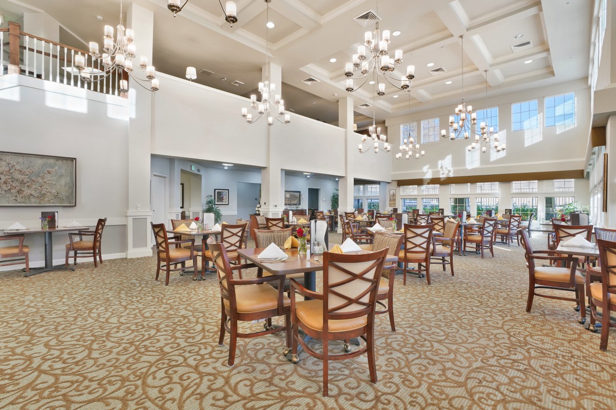 A spacious and elegantly designed dining room with chandeliers, tables, and chairs arranged on a carpeted floor.