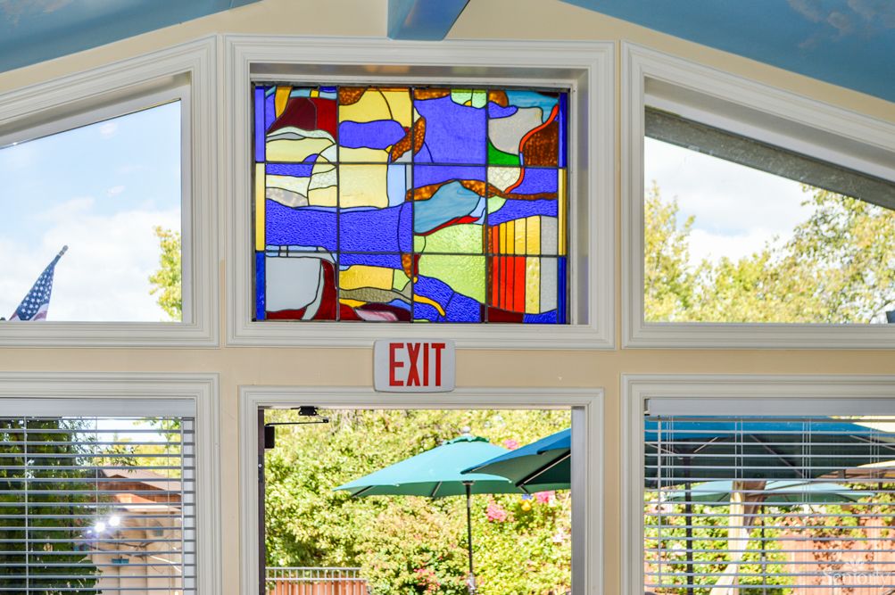Stained glass window with abstract design above an exit in a brightly lit room.