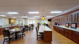 A spacious dining area with wooden tables and chairs, featuring a kitchen and modern lighting.